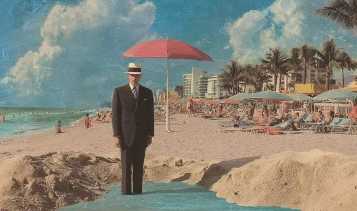 A man standing in the sea next to a red umbrella